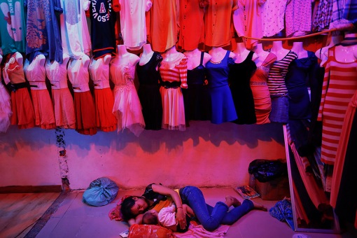 A woman holds her child under cheap dresses offered for sale at a market just outside one of industrial zones in the suburbs of Phnom Penh where many of garment factories are situated