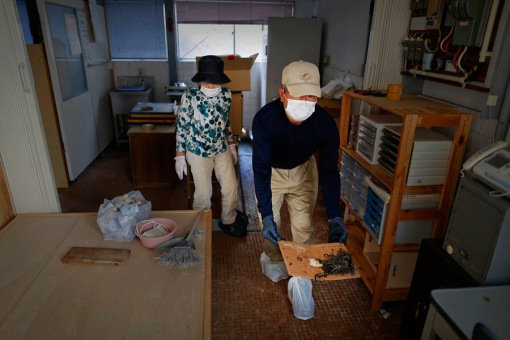Zenjuro Nagaoka is followed by his wife Satoko as he takes a dead mouse out of their sweet shop during a visit to the evacuated town of Namie in Fukushima prefecture