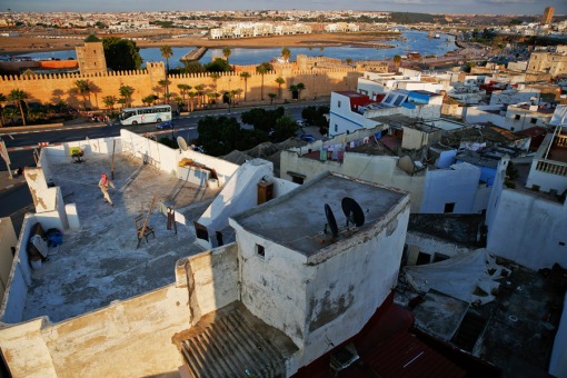 A woman walks of rooftop of a building in Rabat's Medina as the walls of Kasbah of the Oudayas are seen in background